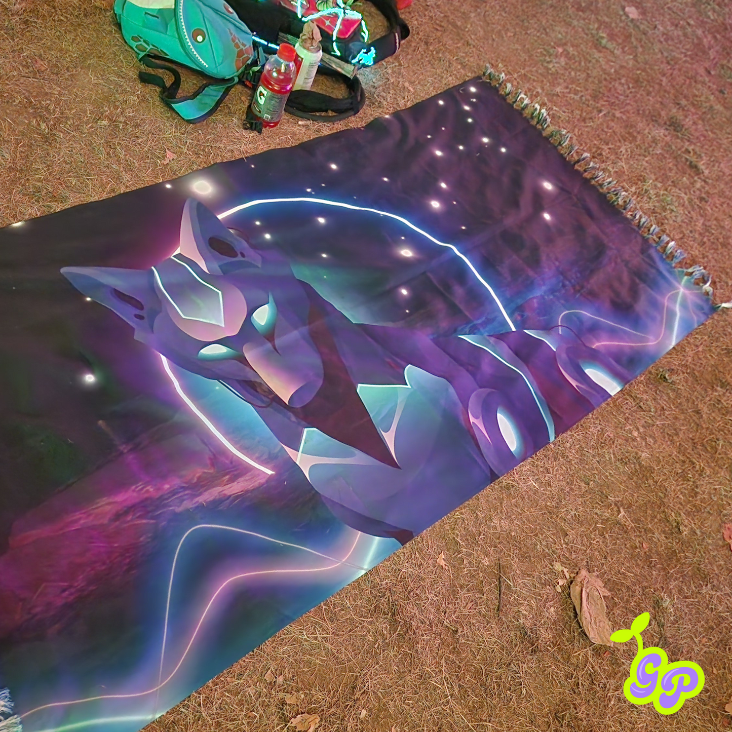 The cyber wolf neon festival pashmina being used in the dirt at a campsite next to a pile of backpacks.