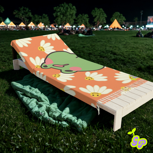 Cartoon frog and smiling daisy print pashmina draped over a white wooden lounge chair on a grassy festival lawn at night.